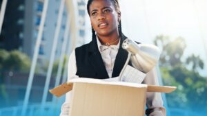 Young professional woman holding a box of office items after a layoff, symbolizing job loss and new beginnings